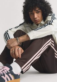 Sportowy strój składający się z białej koszulki w paski i brązowych spodni z różowymi paskami po bokach. Sneakersy w kolorze granatowym z różowymi akcentami i gumową podeszwą.