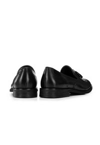 Zapatos de cuero negro con un diseño elegante, que presentan un tacón bajo, punta redondeada y costuras decorativas a lo largo de las costuras.