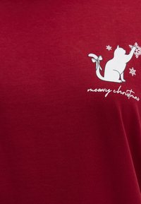Red cotton t-shirt featuring a white cat graphic with a bow, reaching for a snowflake, and the text "meowy christmas" in a playful font.