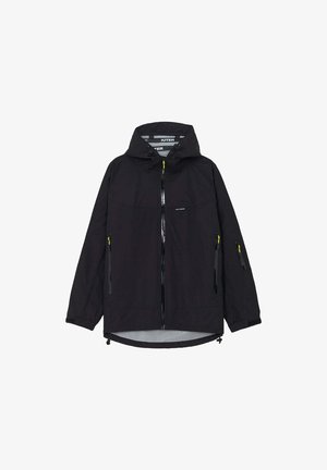 Giacca nera con cappuccio, chiusura frontale con cerniera, due tasche laterali con zip, una piccola tasca con zip sulla manica e dettagli gialli sulle cerniere.