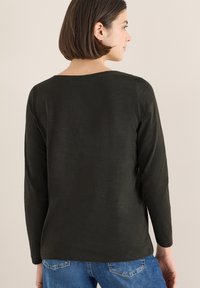 Dark green long-sleeve shirt with a round neckline, relaxed fit, and soft texture, paired with blue jeans. Minimalistic design.