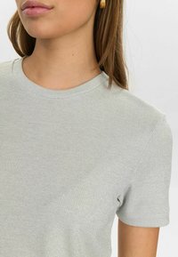 Tricou din tricot ribbed de culoare gri deschis, cu o strălucire subtilă, guler rotund și mâneci scurte. Textură netedă și design ajustat.