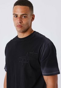 Camiseta de algodón negra de manga corta, que presenta un diseño de logo en relieve en el lado izquierdo del pecho y acentos de costura en contraste.
