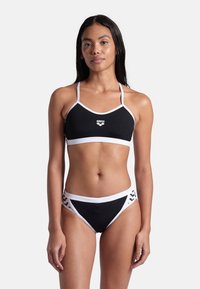 Svart bikini-set med vita detaljer, som har en halterneck-top med tunna band och ett underdel med urklippsdetaljer. Tillverkad av stretcht material för badkläder.