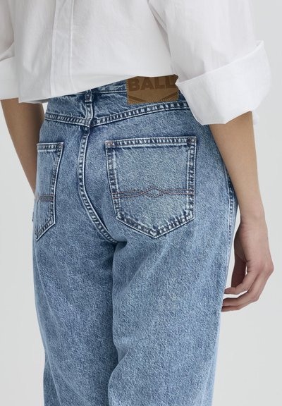 Vaqueros de mezclilla de color azul claro con cintura alta, que cuentan con dos bolsillos traseros y una etiqueta de cuero marrón en la cintura. La textura desgastada realza el diseño.