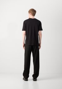 T-shirt noir à manches courtes avec un col rond, associé à un pantalon noir ample. Texture lisse, design minimaliste, sans motifs ni accents visibles.