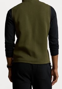 Kamizelka polarowa w kolorze oliwkowym z czarnymi długimi rękawami, z wysokim kołnierzem, gładką fakturą oraz bocznym ściągaczem na dole.