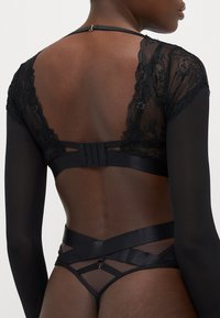 Zwarte kanten en doorschijnende panelen bodysuit met lange mouwen, verstelbare bandjes en een haak-en-oogsluiting op de rug.