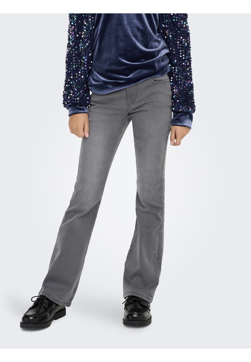 Calças jeans cinzentas flare com textura suave e ligeiro desbotado, combinadas com sapatos pretos de cordões. O conjunto é complementado por um top azul-marinho com lantejoulas.