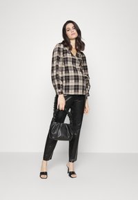 Blusa xadrez preta e bege com babados, combinada com calças de pele sintética pretas e uma bolsa preta franzida. Sapatos de salto abertos pretos.