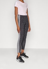 Pink cropped t-shirt with white stripes on shoulders, paired with black leopard-print leggings featuring three white side stripes and black sneakers.