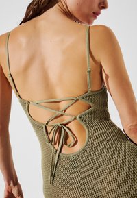 Vestido de punto verde oliva con un diseño entrecruzado en la parte posterior, tirantes ajustables y un detalle de escote redondeado y abierto.