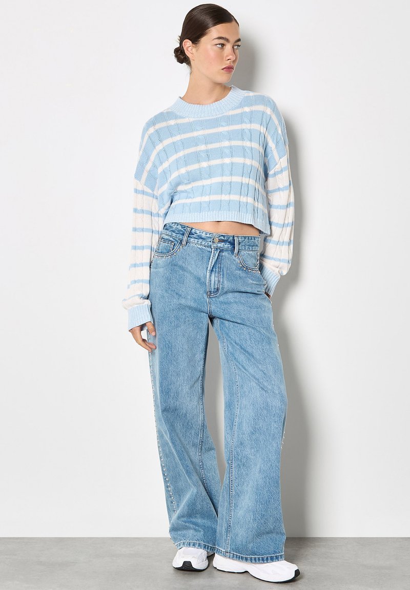Pull court bleu clair avec des rayures blanches et une texture en maille torsadée, associé à un jean large taille haute bleu clair et des baskets blanches.