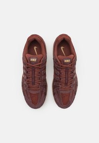 Adidași Nike de culoare roșu închis și burgund cu plasă și nubuc. Caracteristicile includ panouri texturate, accente aurii și un design cu șireturi.