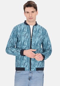 Giacca bomber blu con motivo astratto, polsini e orlo a coste di colore blu navy, chiusura con zip, tessuto leggero, maniche lunghe, interno non foderato.