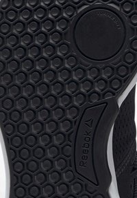 Svart gummisko sula med ett honungskaksmönster, rundade kanter och Reebok-logotyp. Anmärkningsvärd cirkulär detalj nära mitten.