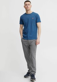 Tricou albastru cu mânecă scurtă, cu o textură dungi fină și un mic logo roșu, asortat cu pantaloni de trening gri și adidași negri.