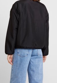 Sort polstret jakke med en afslappet pasform, der har rund hals og lange ærmer, kombineret med lyseblå denim jeans.