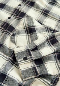 Kreemja ja musta ruudulise mustriga nööbitav flanelliste shirt, pehme tekstuuriga, kraega ja nööbita cuffiga, millel on must nupp.