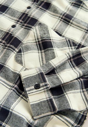 Kreemja ja musta ruudulise mustriga nööbitav flanelliste shirt, pehme tekstuuriga, kraega ja nööbita cuffiga, millel on must nupp.