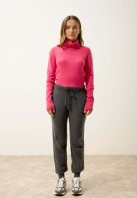 Fuksia turtlenecktröja i mjukt tyg som matchas med grå fleecejoggers med dragsko. Bärs med vita och grå sportskor.