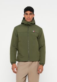 Olive green hooded puffer jacket, zippered front, elastic cuffs, featuring a small logo patch with red, white, and blue details on the chest.