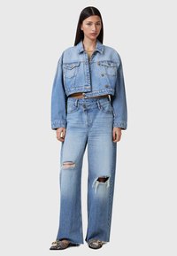 Chaqueta de mezclilla cropped en azul claro y jeans de pierna ancha, con detalles desgastados y un acabado deslavado. Los acentos incluyen botones metálicos.