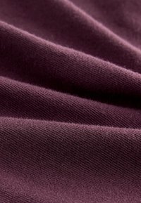 Sügava violetti tooni tekstuuriga kangas, millel on pehme, sile pind, fine niidistik ja õrnad volditud voldid.