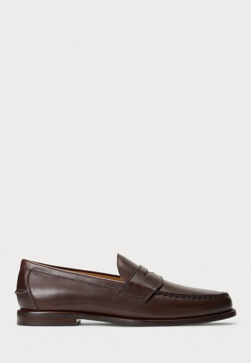 Zapato mocasín de piel marrón oscuro con tacón bajo, punta cosida en forma de mocasín y detalle de tira en la parte superior, exhibido sobre un fondo blanco.