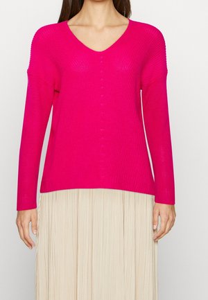 Helderroze gebreide trui met een V-hals, lange mouwen en textuur ribbels. Heeft een relaxte pasvorm en een zachte, rekbare stof.