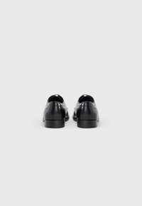 Chaussures en cuir noir à texture lisse, bout arrondi et petit talon. L'arrière présente une découpe courte et des détails de couture minimalistes.