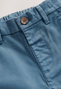 Primo piano della cintura di pantaloni blu con chiusura a bottone, passanti per cintura e parte posteriore elastica per una vestibilità regolabile.
