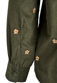 Das olivgrüne Cordhemd verfügt über lange Ärmel mit beiger Blumenstickerei und einen Knopfverschluss am Ärmelbund für sicheren Halt.