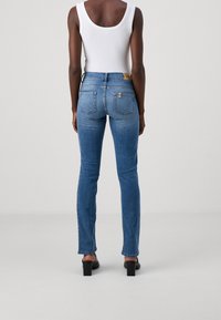 Blå denimjeans med slim fit, medelhögt midjeband och synlig sömnad. Har två bakfickor och en guldtonad logotyp patch.