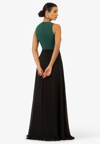 Langes schwarzes Kleid mit einem taillierten grünen Oberteil. Glatte Textur, ärmelloses Design und verdezipper im Rücken. Der schwingende Rock hat einen subtilen Glanz.