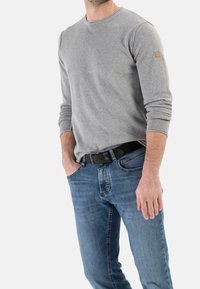 Chemise à manches longues grise en tissu doux, associée à un jean bleu. Détails notables : un col rond et une étiquette sur la manche.