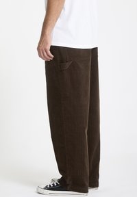 Brune fløjlsbukser med en afslappet pasform, der har en sidelomme og tekstureret stof. Bæret sammen med sorte sneakers og en hvid skjorte.