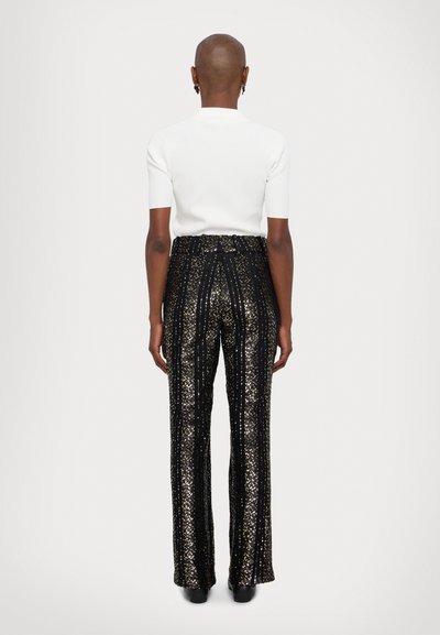 White ribbed short-sleeve top paired with black sequin flared pants featuring gold stripes. The outfit has a fitted waist and flared hem.