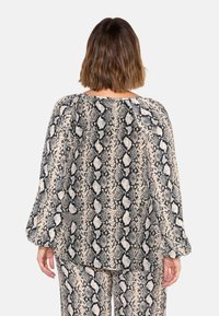 Blouse à manches longues en tissu imprimé serpent, avec une coupe ample, un col rond et un motif texturé noir et neutre.