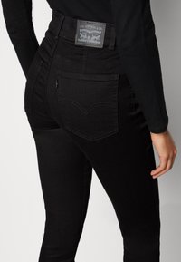 Svarta denimjeans med hög midja, subtila sömmar och en etikett på baksidan. Slimmad design, inkluderar bakfickor med svängda sömmar.