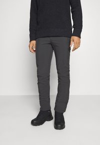 Pantalons slim gris foncé, fabriqués à partir d'un matériau léger et flexible. Associés à des bottes de randonnée noires, avec une surface texturée et des détails en dentelle.