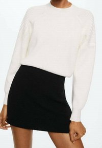 Pull à côtes blanc avec un col rond et des manches longues, associé à une mini-jupe noire ajustée. Les deux vêtements présentent des textures lisses.