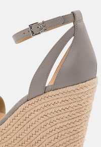 Sandale en coin grise avec une semelle en jute tissée, un dessus en cuir lisse, un design de languettes entrecroisées et une fermeture à boucle métallique.