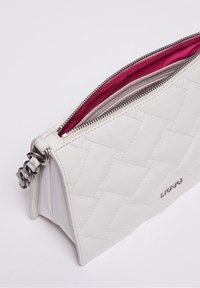 Valkoinen tikattu nahkalaukku, jossa on hopeinen vetskari osittain auki, paljastaen punaisen kankaan sisäosan ja hopeaketjun hihnan yksityiskohdan.