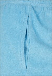 Gros plan d'un tissu en éponge bleu clair avec une ouverture verticale, montrant la texture et les détails des plis.