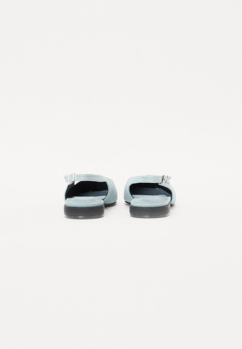 Lichtblauwe, suede instapschoenen met een open achterkant, platte zwarte rubberen zool en een zilveren metalen gespdetail. Eenvoudig ontwerp en textuur.