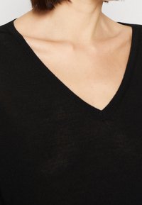 Czarny sweter z dekoltem w serek o miękkiej fakturze. Posiada ryflowany dekolt i ramiona, prezentując zbliżenie na tkaninę i fason.