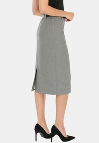 Szara spódnica ołówkowa z bocznym rozcięciem, wykonana z teksturowanej tkaniny. Posiada pasek na pasie i długość do kolan. Noszona z czarnymi szpilkami.