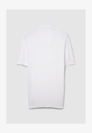 Polo blanc à manches courtes, présentant une texture côtelée, un col standard et un motif de tricot subtil, offrant un design épuré et minimaliste.