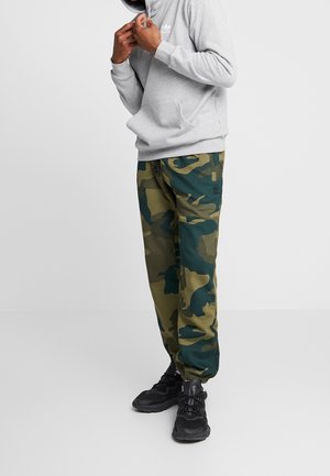 Sudadera gris con un bolsillo frontal, combinada con pantalones de camuflaje verdes y azules que tienen una cintura con cordón y puños elásticos, usados con zapatillas negras.